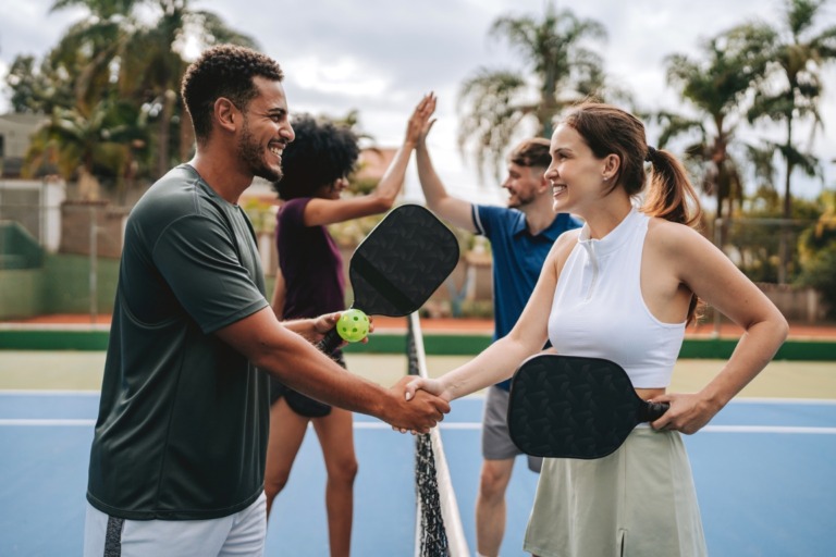 Group of friends playing pickleball on an outdoor court, smiling and engaged in a lively game.