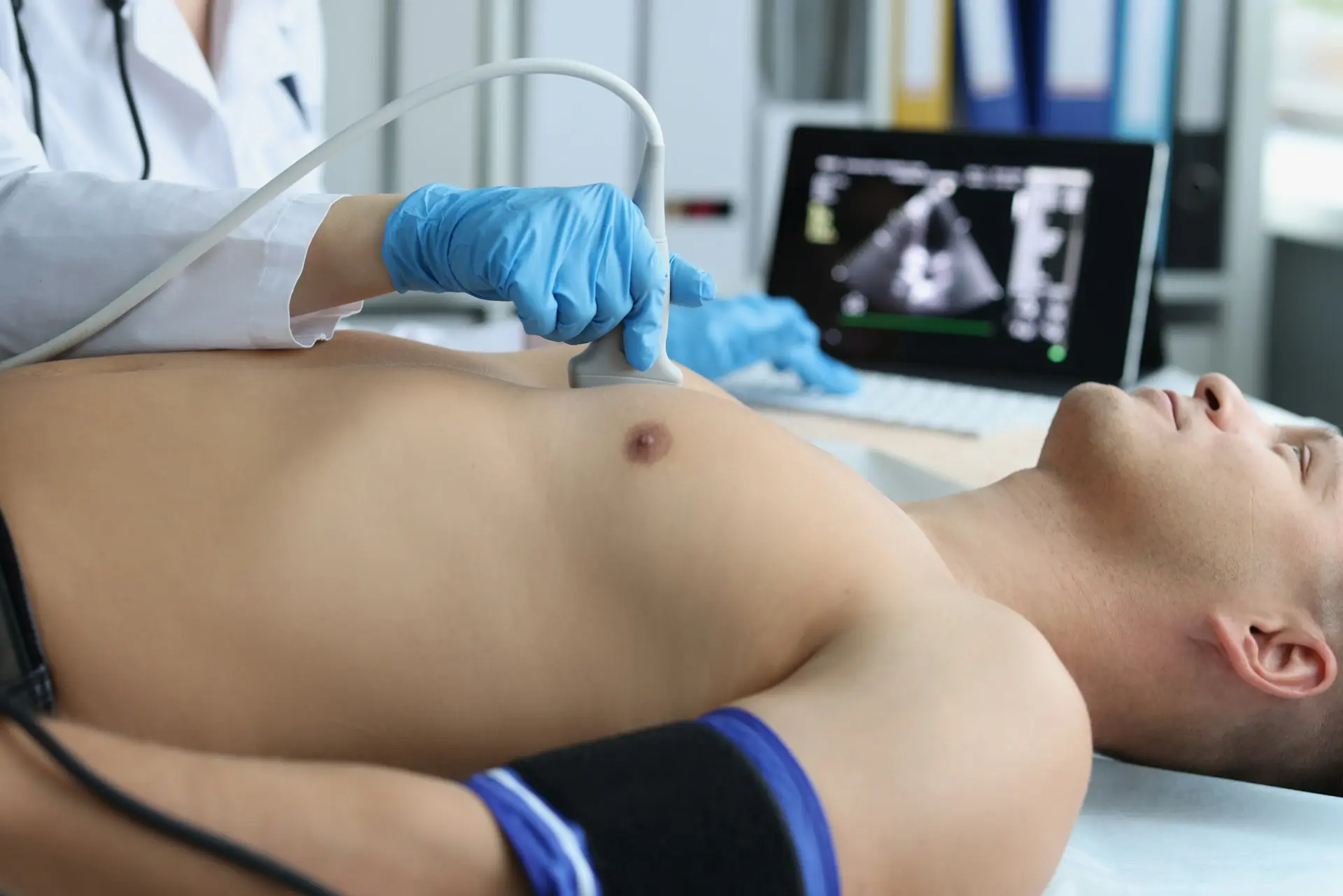 Medical professional performing musculoskeletal ultrasound imaging on a patient’s chest with the scan displayed on a monitor.