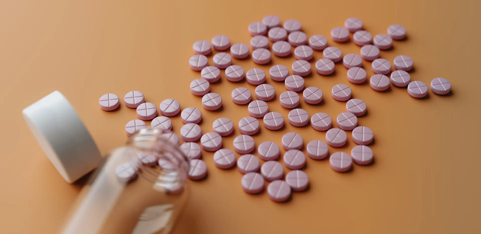 Numerous tablets arranged on a surface with a medicine bottle nearby, representing cholesterol-lowering statin medications.