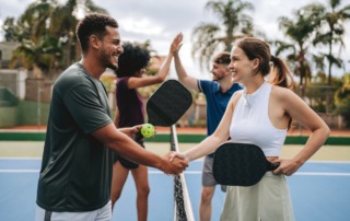 Group of friends playing pickleball on an outdoor court, smiling and engaged in a lively game.