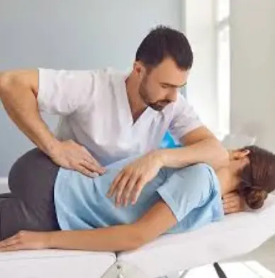 A healthcare provider performs osteopathic manipulative treatment on a patient lying on their side on an exam table. The practitioner places one hand on the patient's back and the other on the shoulder area, positioning the body to apply controlled manual pressure to the spine or surrounding muscles.