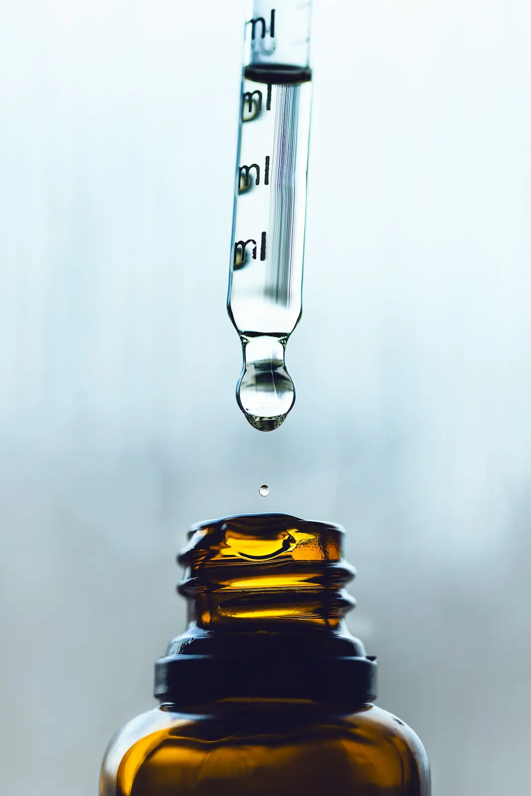 Glass dropper above an amber bottle with a drop of oil, representing cannabinoid tincture or CBD oil.