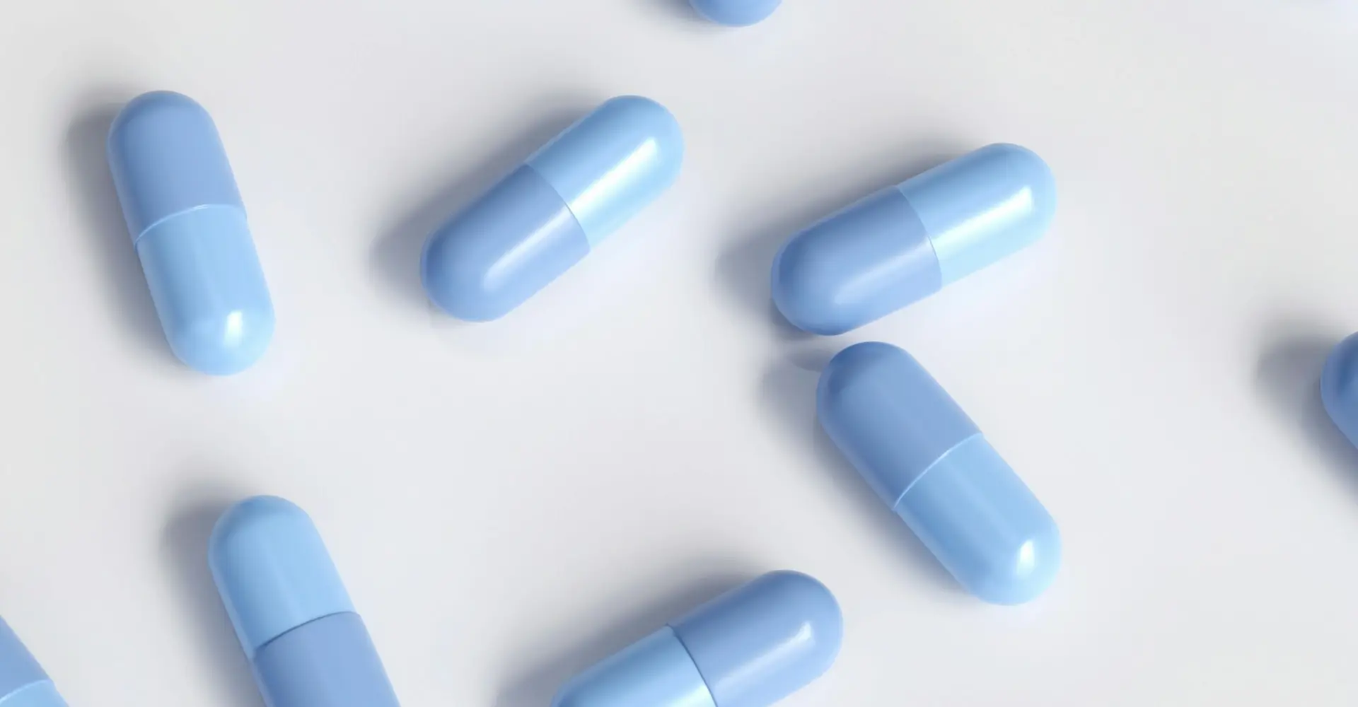 Several light blue medication capsules scattered randomly on a white surface, shown in a close-up overhead view.